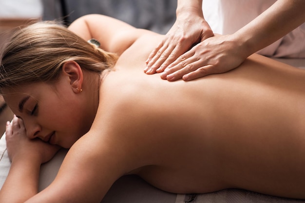 Masseur massaging back and shoulder blades of young woman on massage table Concept of massage spa treatments Closeup