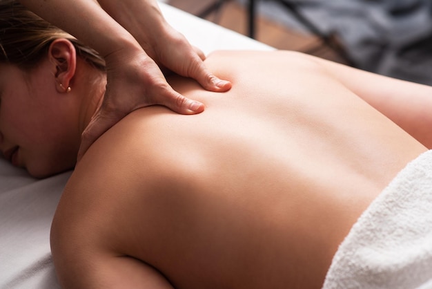 Masseur massaging back and shoulder blades of young woman on massage table Concept of massage spa treatments Closeup