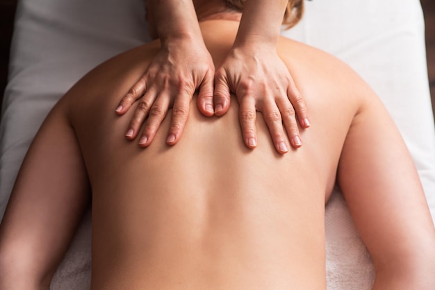 Masseur massaging back and shoulder blades of young woman on massage table Concept of massage spa treatments Closeup