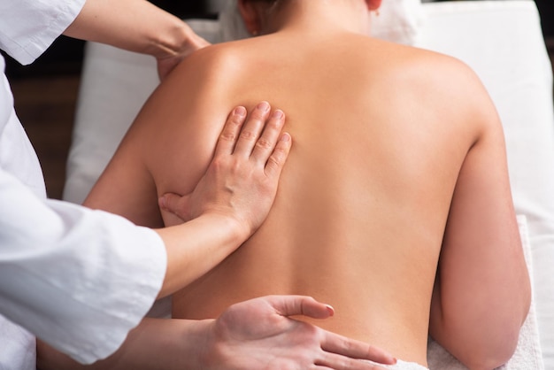 Masseur massaging back and shoulder blades of young woman on massage table Concept of massage spa treatments Closeup