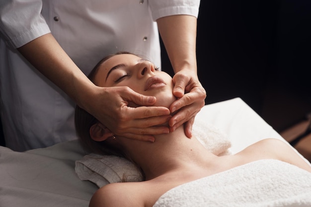 Masseur massaging decollete and neck of young woman on massage table Concept of massage spa treatments Closeup