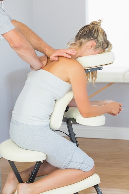 Masseur treating clients shoulder in massage chair