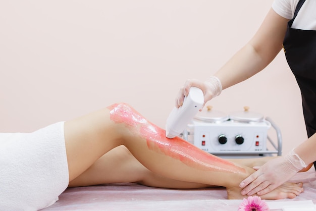 A master applies pink depilatory wax to a young woman's leg for hair removal Depilation with wax