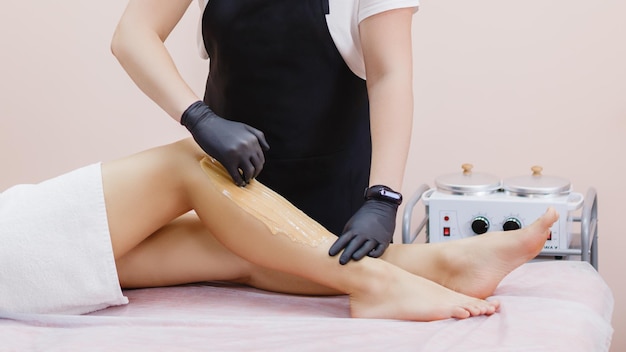 A master applies a shugaring paste to a young woman's leg to remove hair Sugaring Depilating legs