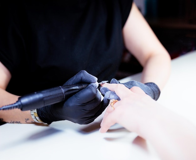 The master in black gloves uses an automatic electric nail polish remover for women.