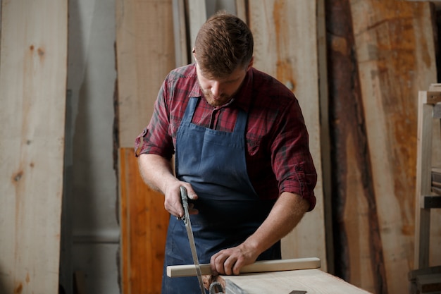 Master carpenter saws board with a hacksaw in the workshop