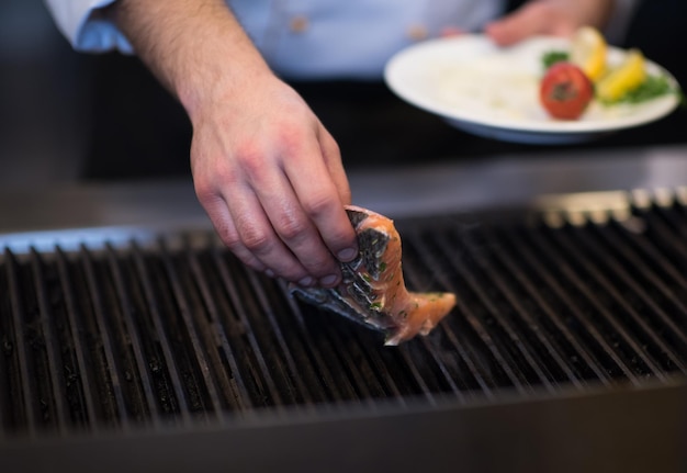 Master chef hands cooking grilled salmon fish with potatoes on a restaurant kitchen