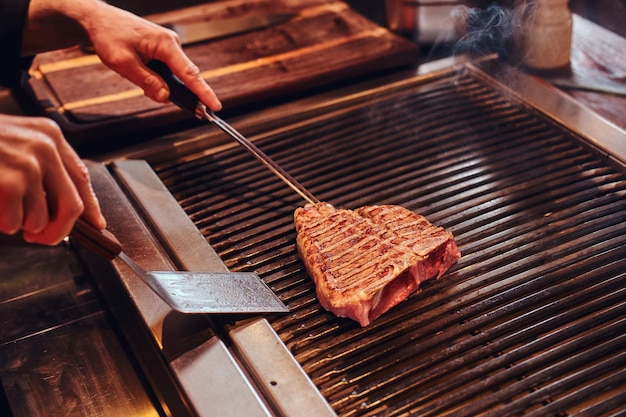 Master chef wearing uniform cooking delicious beef steak on a kitchen in a restaurant