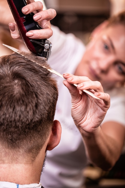 The master cuts the hair and beard of a man in a barbershop, a hairdresser does a haircut for a young man. Beauty concept, self care.