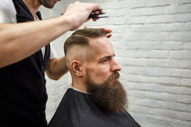 Master cuts hair and beard of man in the barbershop