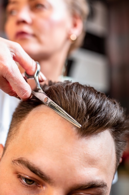 Master cuts man's hair in the salon. Scissors, Roschetsk close-up. Concept hairdressing, haircut, beauty.