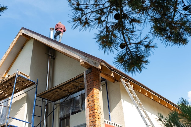 The master for the installation of ventilation pipes and the installation of the chimney of the furnace works on the roof of the house