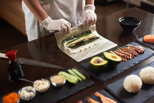 Master making a sushi roll with nori, rice, cucumber and omelet using bamboo mat