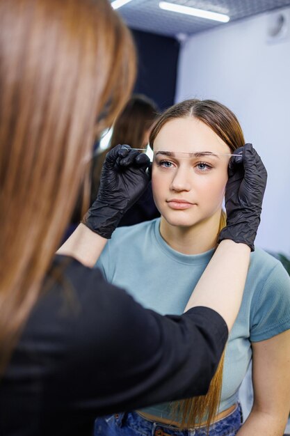 The master marks the woman's face before permanent eyebrow makeup Eyebrow tattoo Beauty procedure for a woman's face