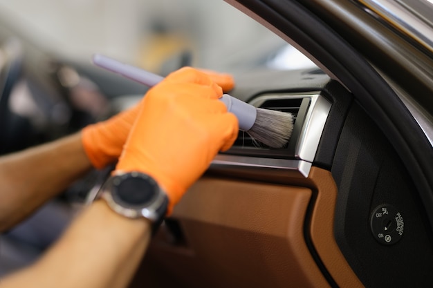 Master mechanic in rubber gloves wiping air conditioner of car with brush closeup