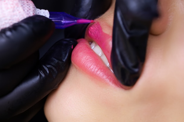 The master of permanent makeup performs a tattoo on the beautiful lips of a young model