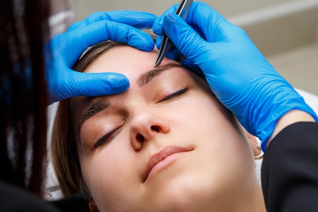 The master plucks out the excess hairs on the eyebrows with tweezers, giving them a shape.