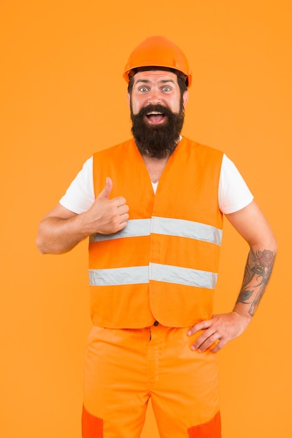 Photo master of quality. master builder showing thumbs up on orange background. bearded man master happy smiling in protective helmet and safety vest. master of building.