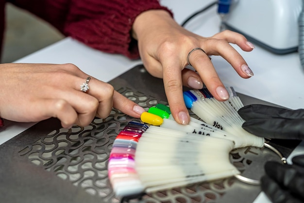 A master in rubber gloves and a young female client in a protective mask choose a color for a manicure in the interior of a beauty studio Manicure and pedicure salon covid19 and social distance