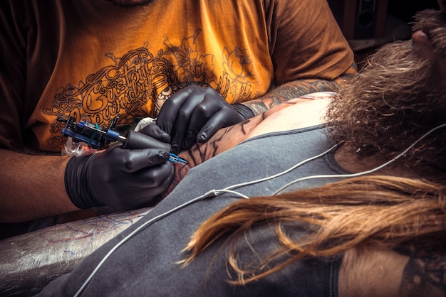 Master showing process of making a tattoo in tattoo studio.