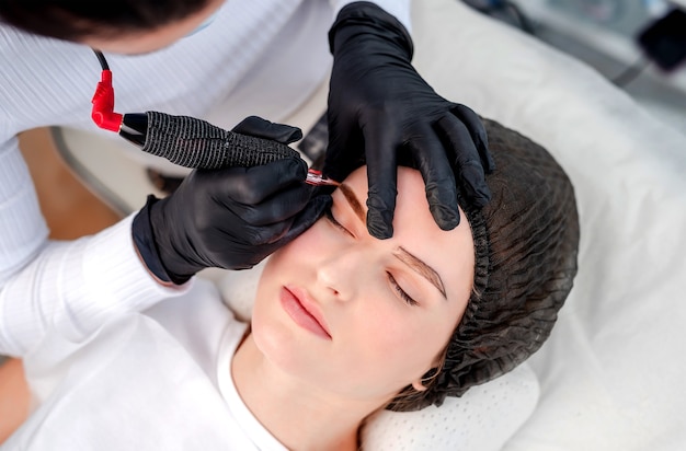 Master using professional microblading machine with inks and needle making beautiful eyebrows permanent makeup