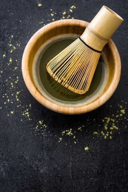 Photo matcha green tea in a bowl and bamboo whisk on black slate