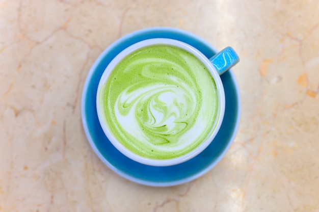 Matcha green tea latte with a pattern of milk foam in a blue ceramic cup on the table