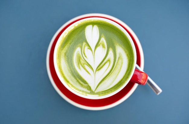 Matcha latte green milk foam red cup on blue table at cafe Trendy powered tea trend from Japan