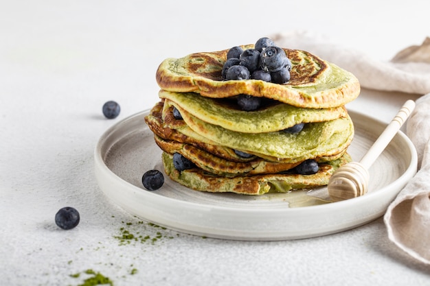 Matcha pancakes on a white table with blueberries and honey vegan food