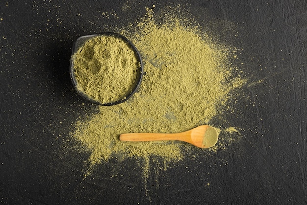 Matcha tea powder in a bowl and spread out on a black table