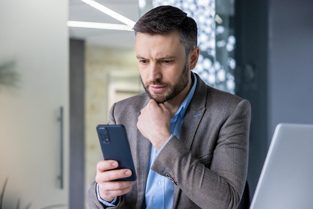 Mature adult businessman close up thoughtfully looking at phone screen man thinking reading social