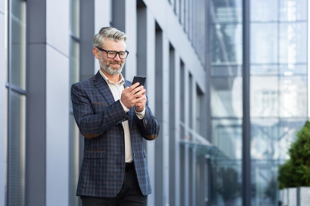 Mature adult businessman outside office building walking and using smartphone boss typing message in