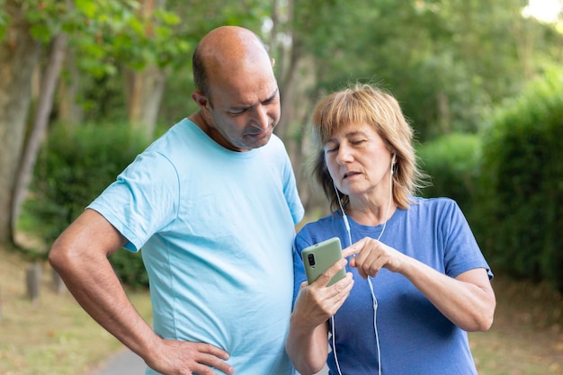 Mature adult couple strolling through the park while the woman shows the husband a photo on her mobile phone