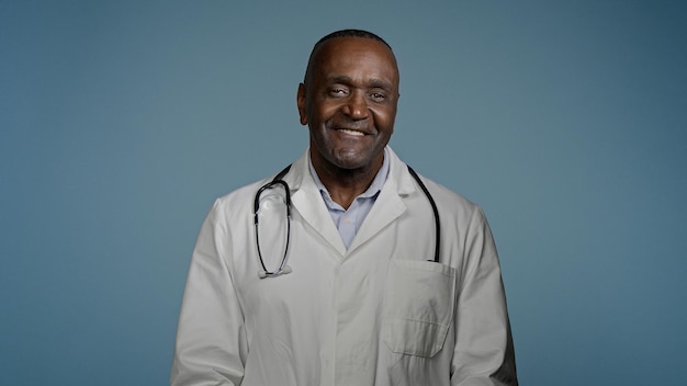 Mature african american man doctor stand in blue background studio in protective mask in medical