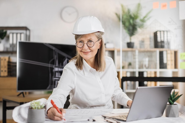 Mature architect woman or female builder sitting on the desk at workplace in modern office