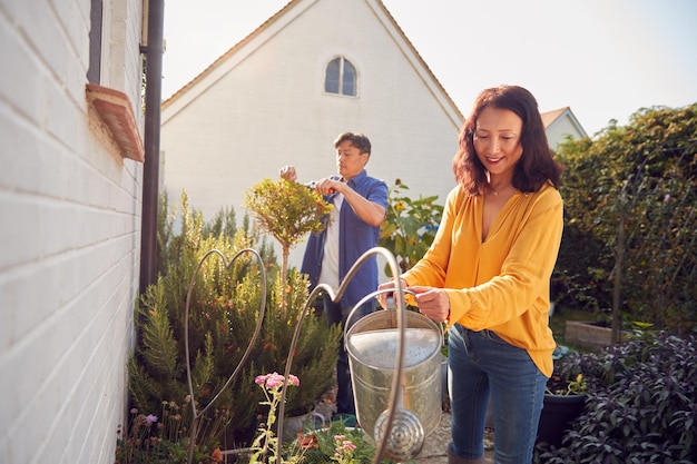 Mature Asian Couple At Work Watering And Pruning Plants In Garden At Home