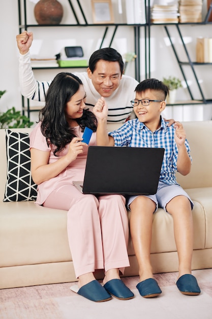 Mature Asian woman buying present online for her excited husband and preteen son