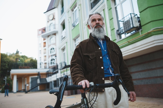 Mature bearded man walking city street with a bicycle beside him