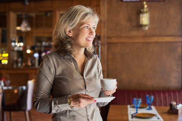 Mature beautiful woman in restaurant with cup of coffee. Businesswoman resting during break, copy space