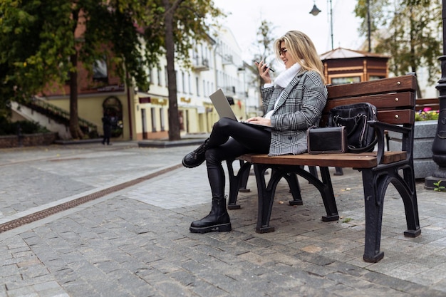 Mature business woman in the park on a bench with a laptop on her knees speaks via video link