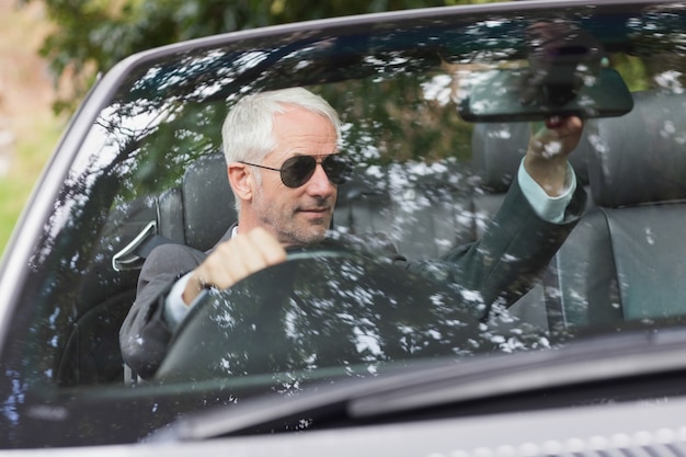 Mature businessman adjusting his cabriolet rear view mirror