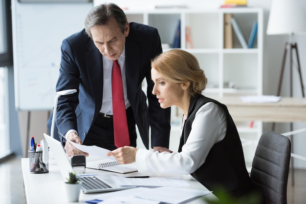 Mature businessman and blonde businesswoman discussing documents at workplace