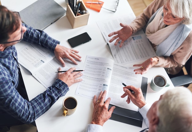 A mature businessman and businesswomen planning contracts with their coworker A senior couple meeting their banker to discuss and plan their retirement from above A mature couple signing contracts