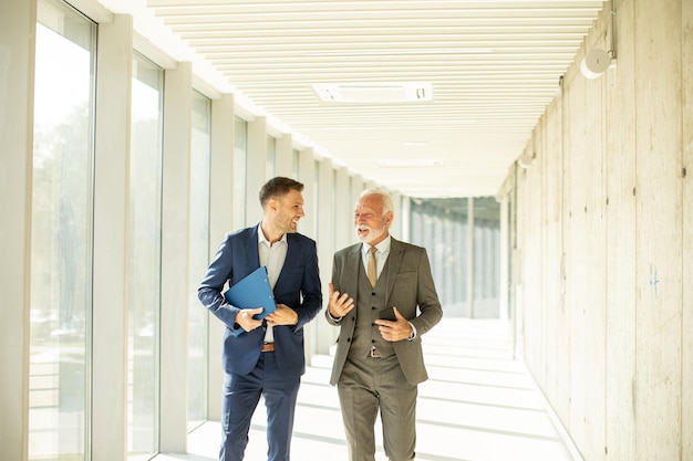 Mature businessman and his young colleague discussing financial report in the office corridor