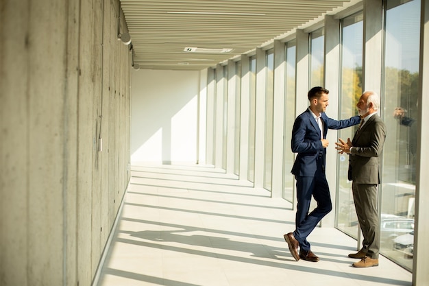 Mature businessman and his young colleague discussing in the office corridor