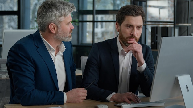 Mature businessman mentoring man discussing project on computer consulting investor client about