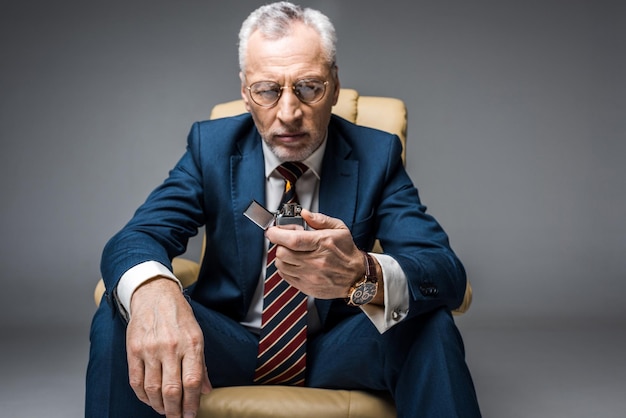 Mature businessman in suit looking lighter with fire on grey