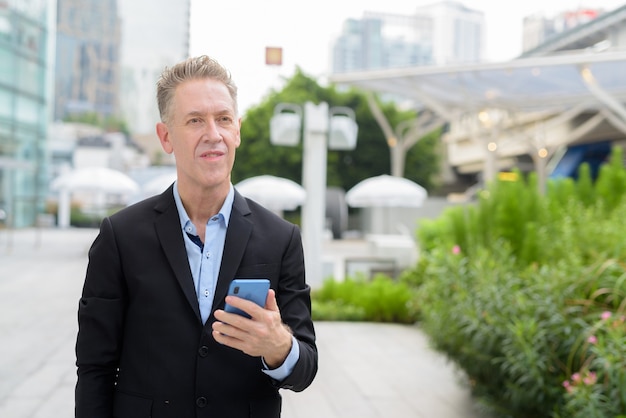 Mature businessman thinking while using phone in the city streets outdoors