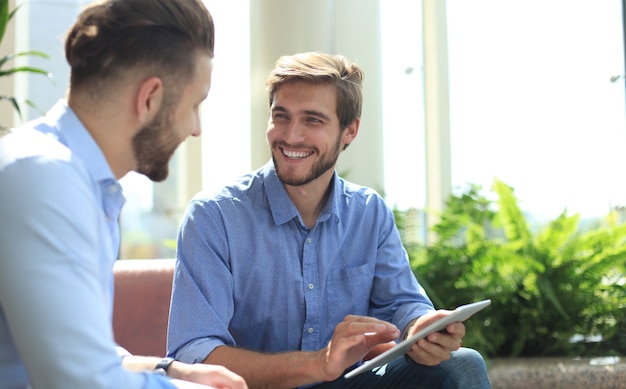 Mature businessman using a digital tablet to discuss information with a younger colleague in a modern business office