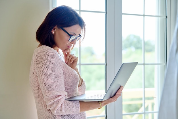 Mature businesswoman in glasses with laptop in her hands near window